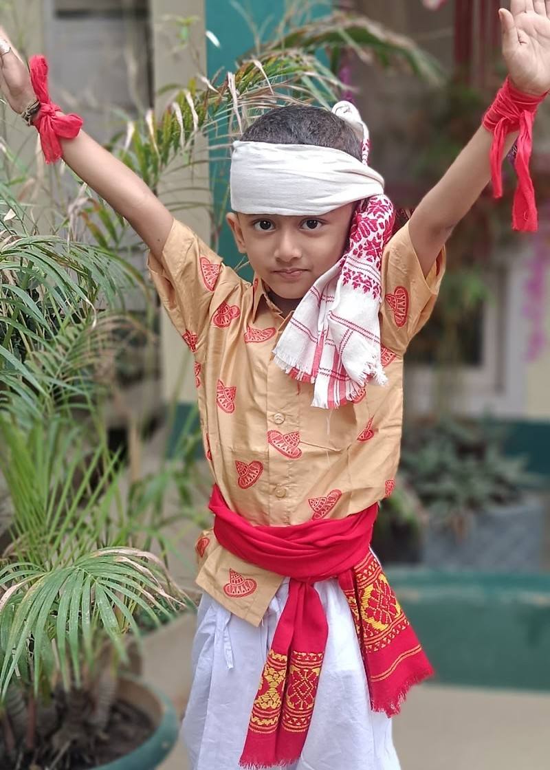 A child in a traditional costume with a red sash raises both arms happily during a school event