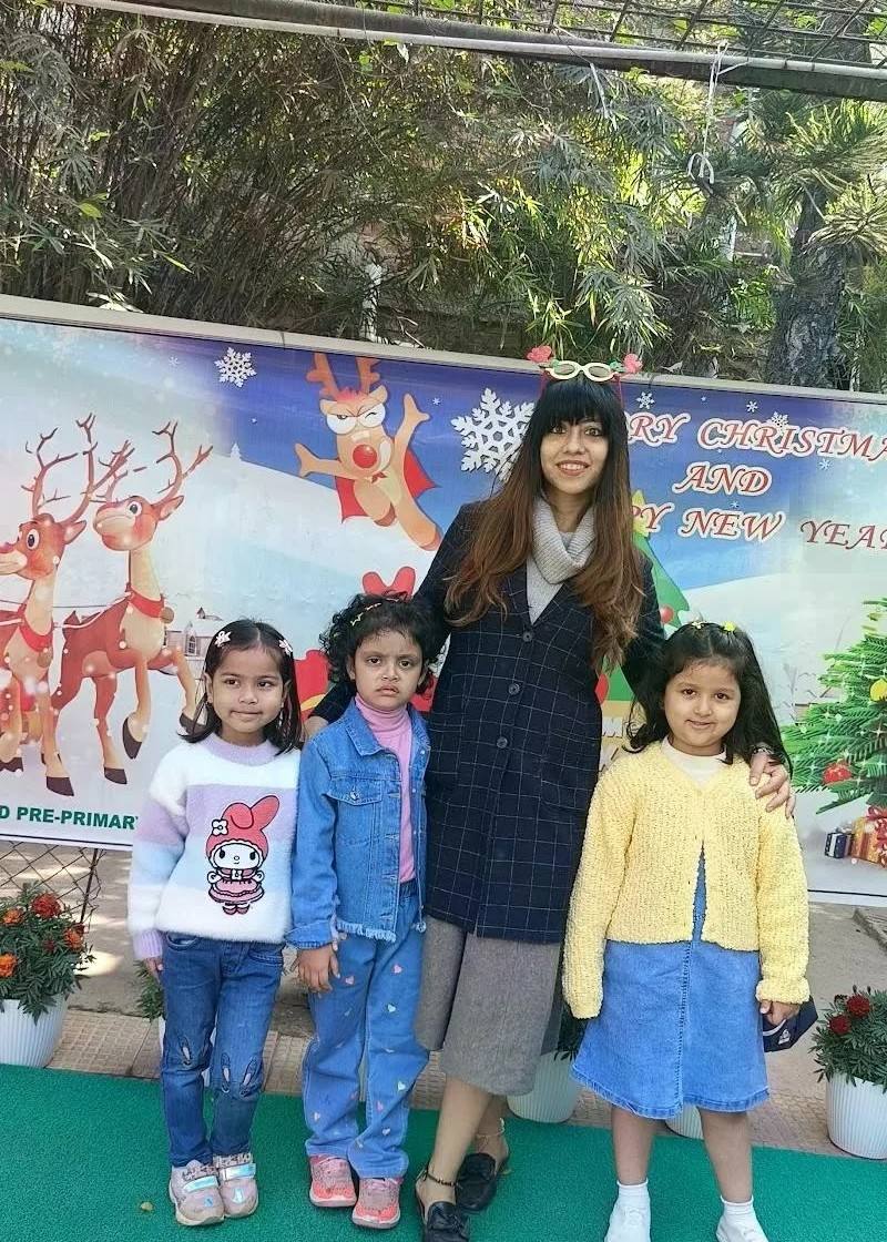 Three young girls and a woman smiling in front of a Merry Christmas and Happy New Year backdrop with reindeer